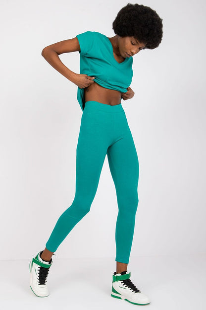 Close-up view of a fashionable model adjusting her matching teal top while wearing BFG Luxury Cotton-Spandex Leggings, highlighting the comfortable elastic waistband and sleek silhouette.