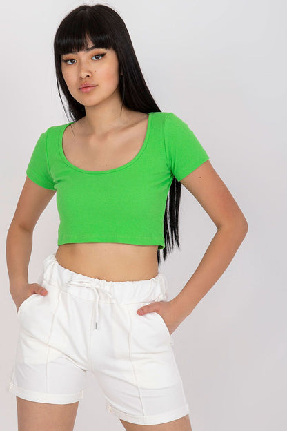 Model showcasing luxury cotton high-waisted shorts with tie waist and pockets in white, complemented by a vibrant green crop top, epitomising modern luxury. EU Size 0.