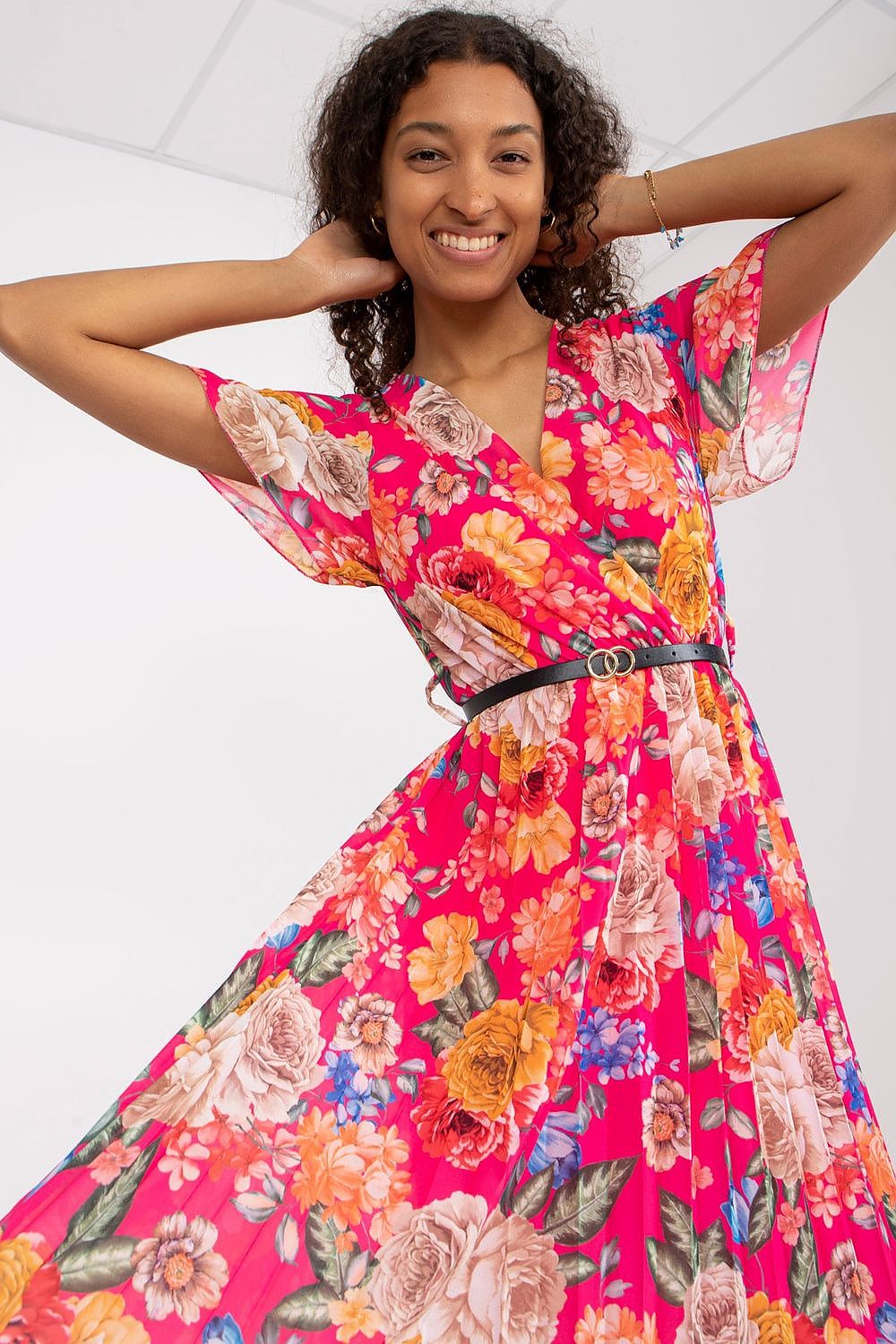 Floral Summer Dress with Belt and Pleated Hem by Italy Moda - Elegant Flared Design. A joyful model smiles in a striking pink floral dress with flowing fabric, showcasing the elegant design suitable for summer occasions.