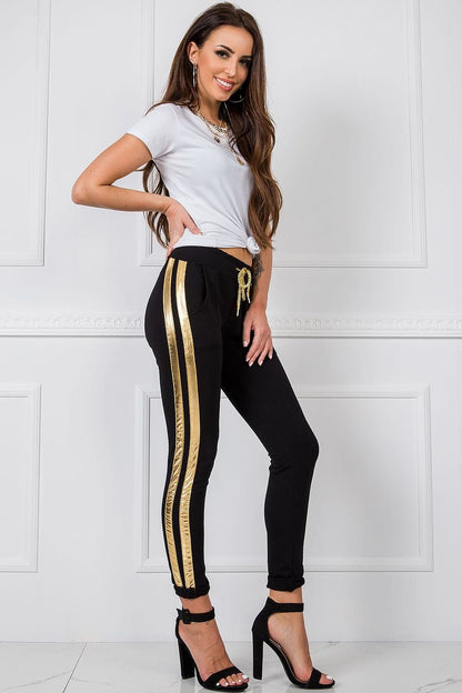 Luxury Women's Tracksuit Trousers with Elastic Waistband and Contrasting Side Stripes, a chic model displaying black tracksuit trousers with gold stripes and a trendy white top, for a sophisticated appearance.