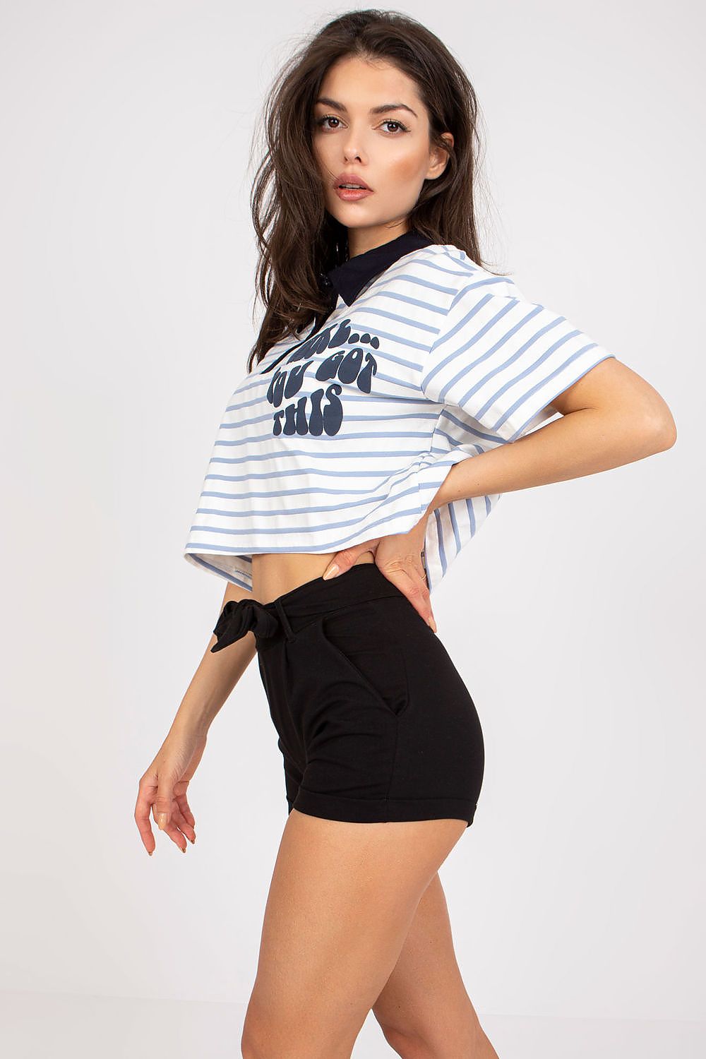 Sophisticated pose of a model wearing the Stylish Striped Cotton Polo Blouse with Decorative Print - EU Size 0, highlighting the luxurious cotton blend fabric and bold decorative print, complemented by chic black shorts.