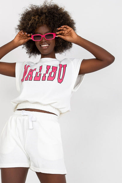 Ex Moda Cotton Blend Tracksuit Set with Blouse and High-Waist Shorts, Stylish and Comfortable. Model with an elegant afro hairstyle, wearing a white blouse and shorts set adorned with 'MALIBU' print, complemented by pink sunglasses.