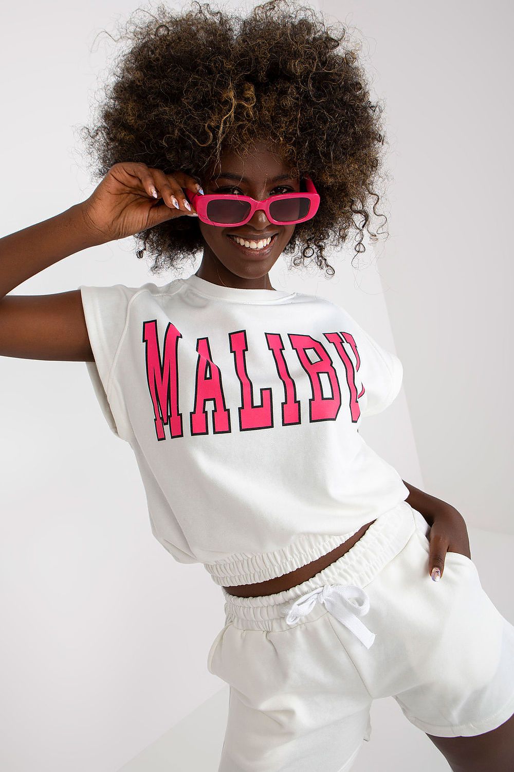 Stylish model wearing the Ex Moda Cotton Blend Tracksuit Set, highlighting the blouse with 'Malibu' inscription and high-waist shorts for a luxurious casual look.