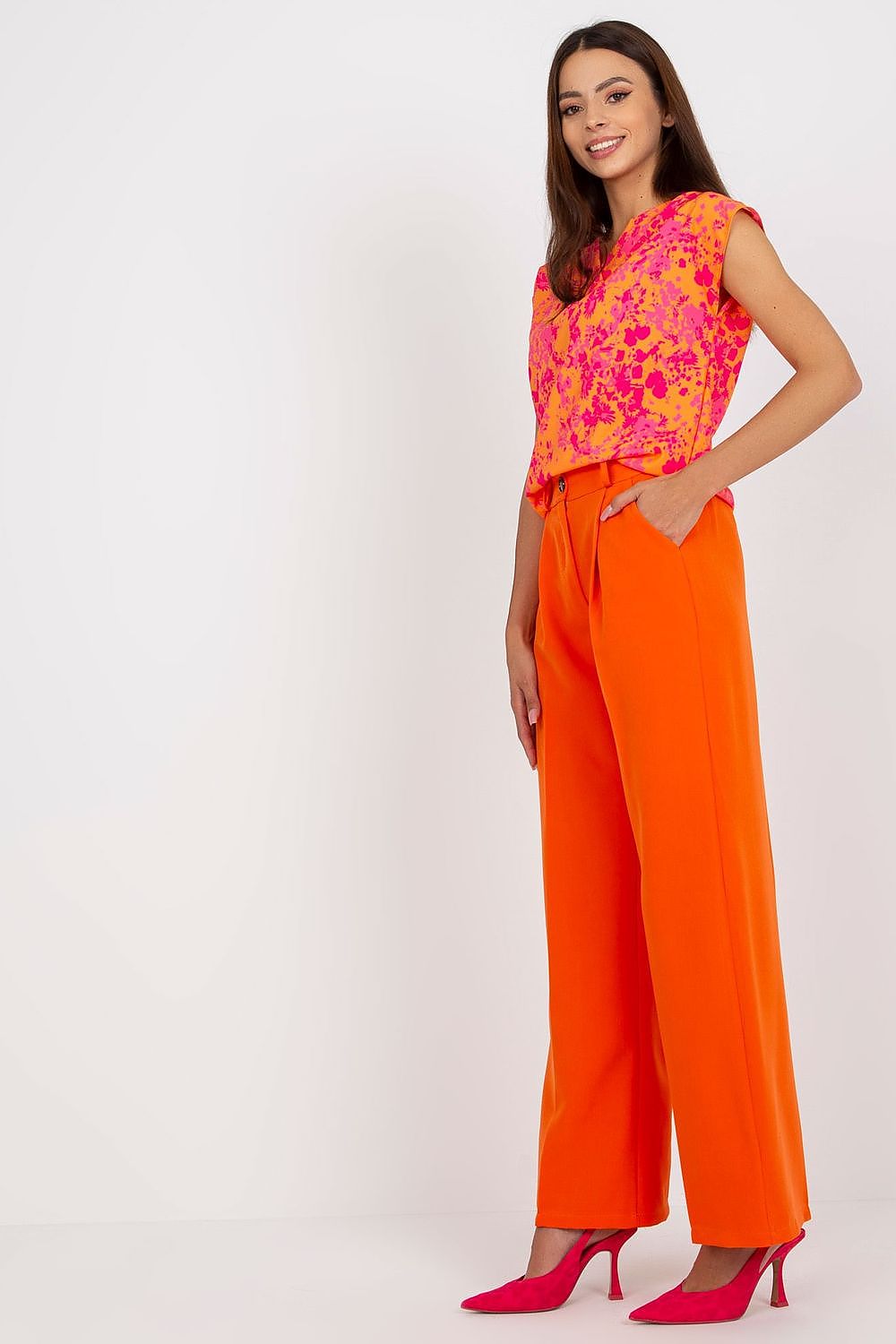 Luxury Women’s Italy Moda Trousers - High Rise Fabric Pants with Zip and Button Fastening, displayed by a model from a side angle, wearing striking orange trousers with a pink floral top.