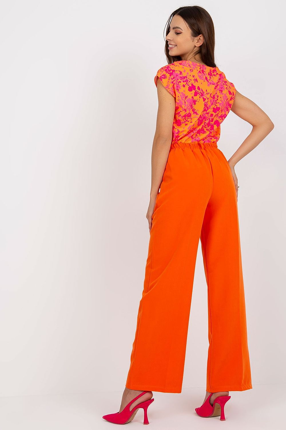 Luxury Women’s Italy Moda Trousers - High Rise Fabric Pants with Zip and Button Fastening, featuring a model wearing orange trousers while showcasing the back view with a vibrant pink floral top.