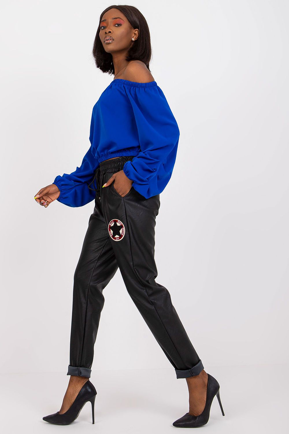 Dynamic shot of a stylish model wearing Luxury Women's Ecological Leather Trousers with Elastic Waistband by Italy Moda, featuring an off-shoulder blue blouse, exuding elegance.