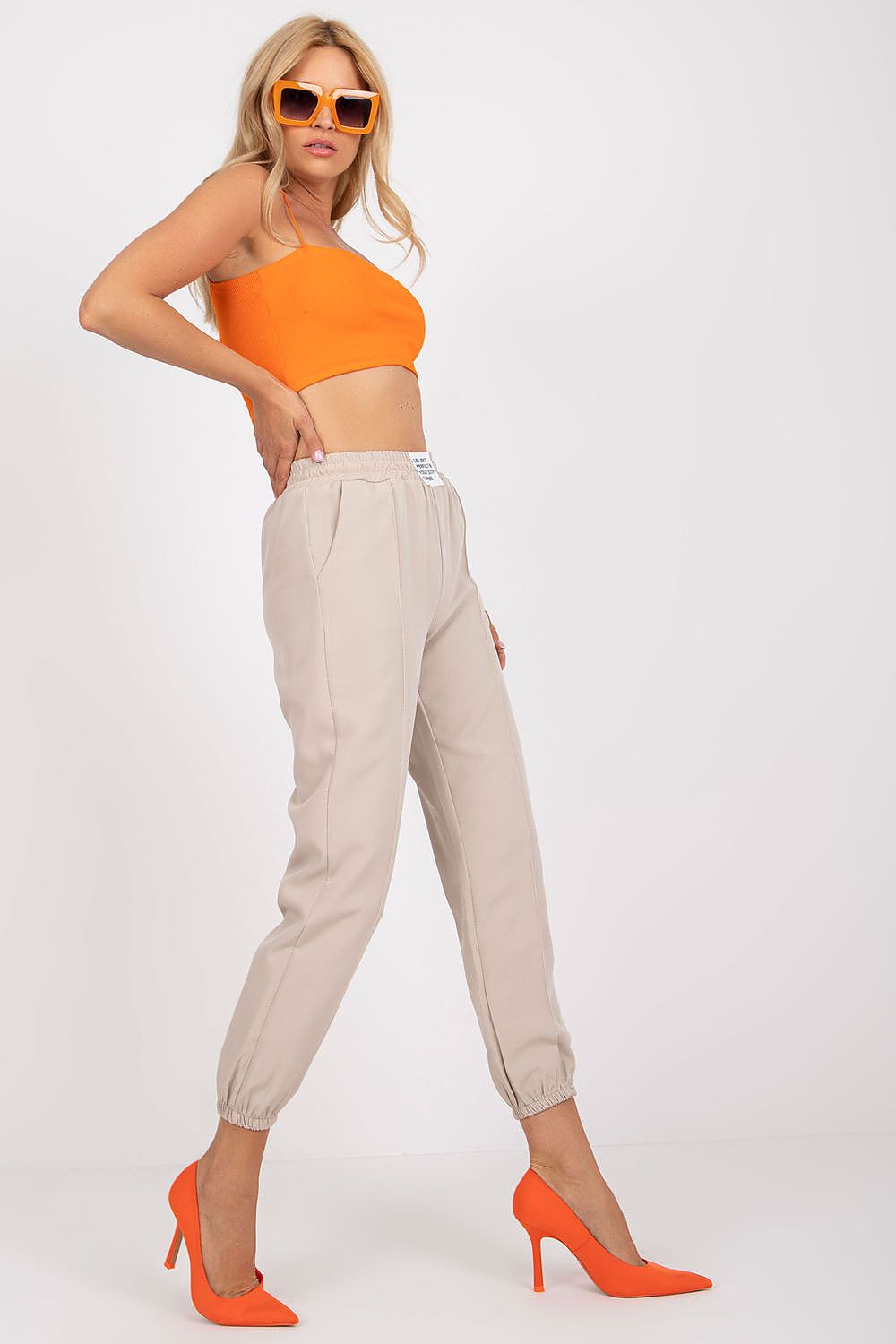 Fashionable women's luxury high-rise trousers with elastic waist and pockets by Italy Moda, styled with an eye-catching orange crop top and oversized sunglasses, accentuating a modern look.