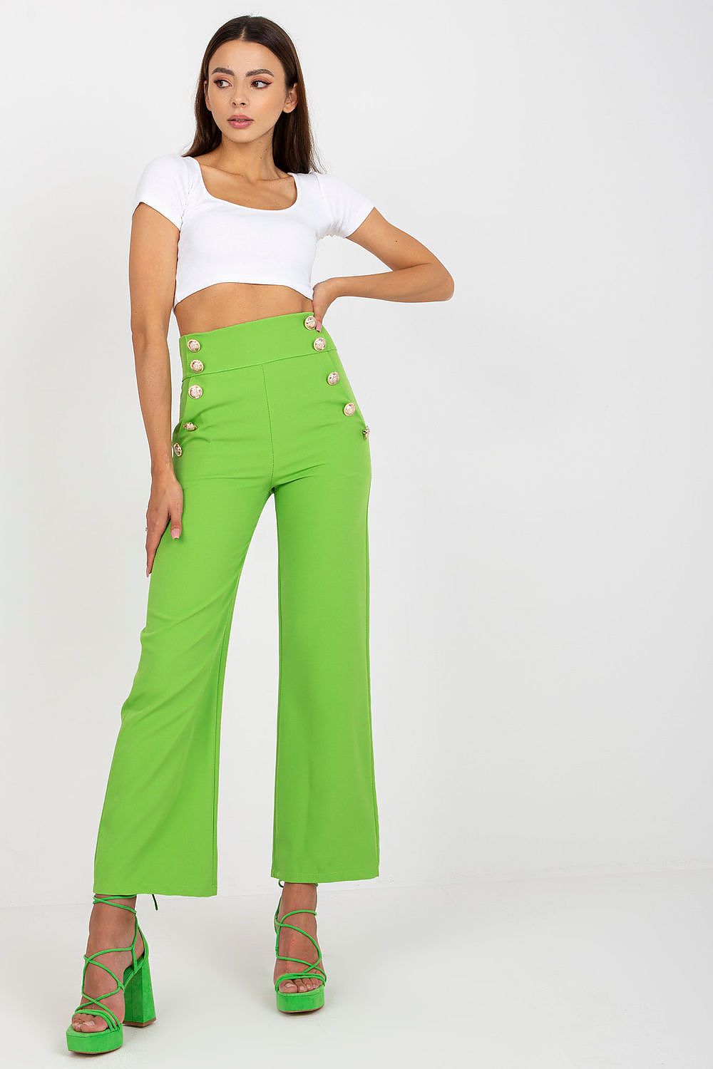 Trendy high-waisted trousers with decorative buttons by Italy Moda, worn by a model in vibrant green paired with a cropped white top.