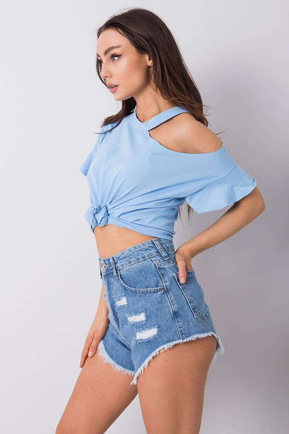 Sophisticated side view of a model demonstrating the stylish off-shoulder cotton blend blouse with short sleeves in blue, knotted at the waist with ripped denim shorts for a fashionable ensemble.