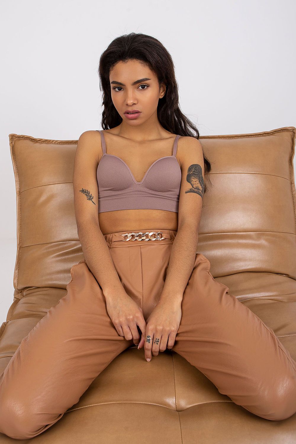 Luxury Women's 7/8 Eco Leather Trousers with High Rise and Decorative Chain by Italy Moda, model seated on a couch, demonstrating chic comfort in fashion.