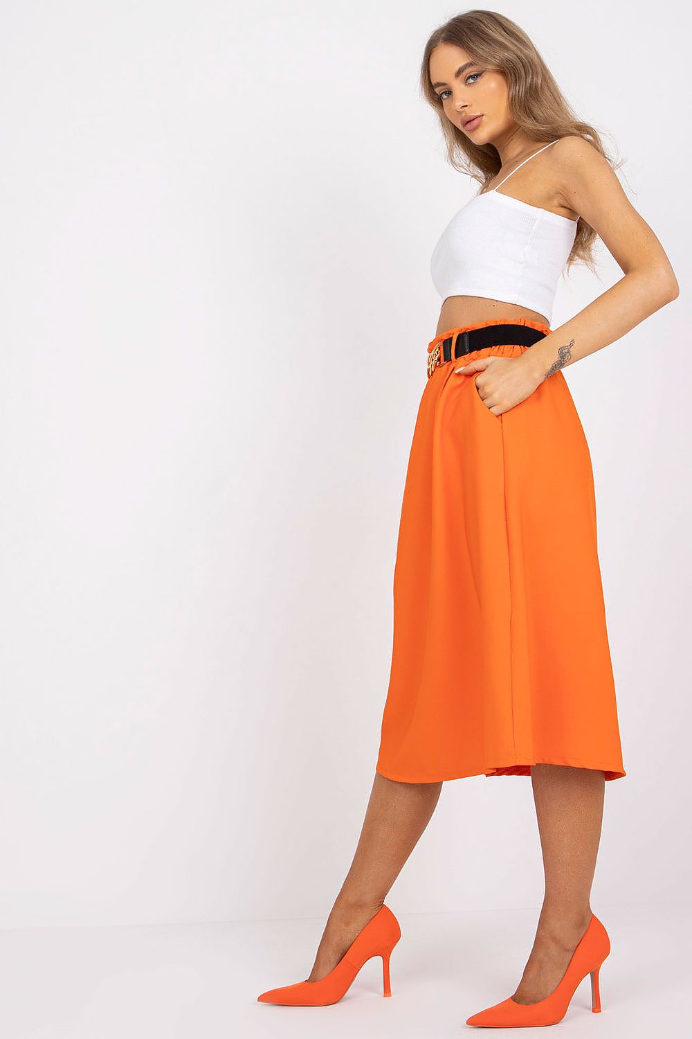 Elegant Italy Moda Skirt with Elastic Waistband, Side Pockets & Decorative Belt shown on a model in a dynamic pose, complemented by sophisticated orange stilettos, highlighting its luxurious appeal.