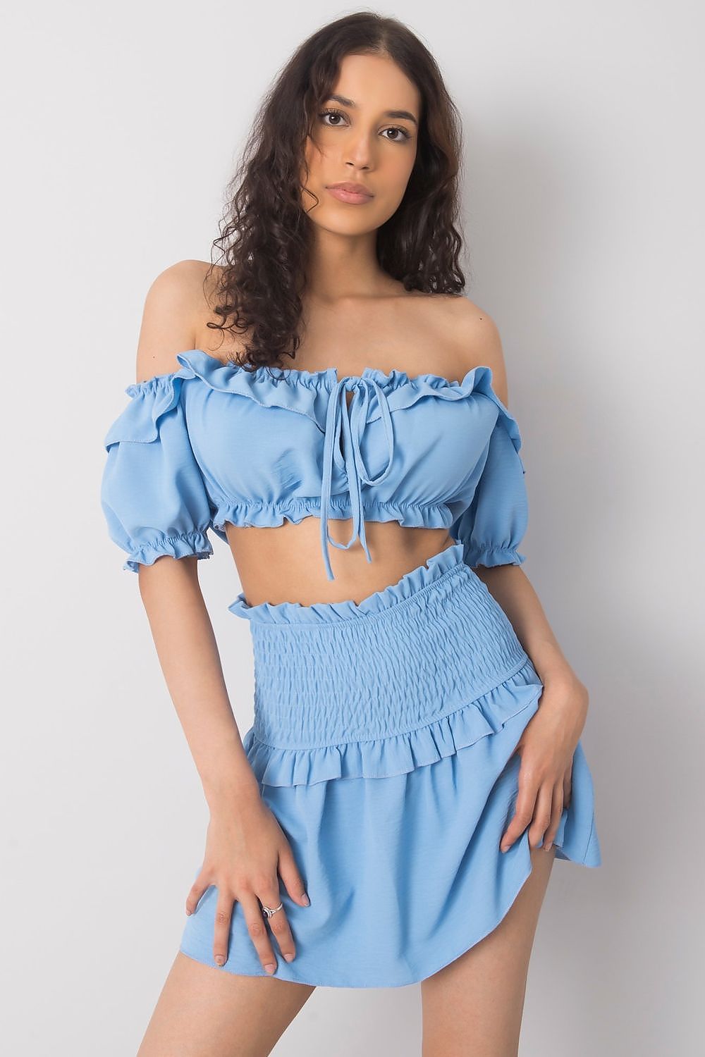 A model elegantly wearing the Och Bella Women's Short Summer Skirt with Wide Elastic Waistband in a soft blue colour, paired with a matching off-the-shoulder top, perfect for summer occasions.