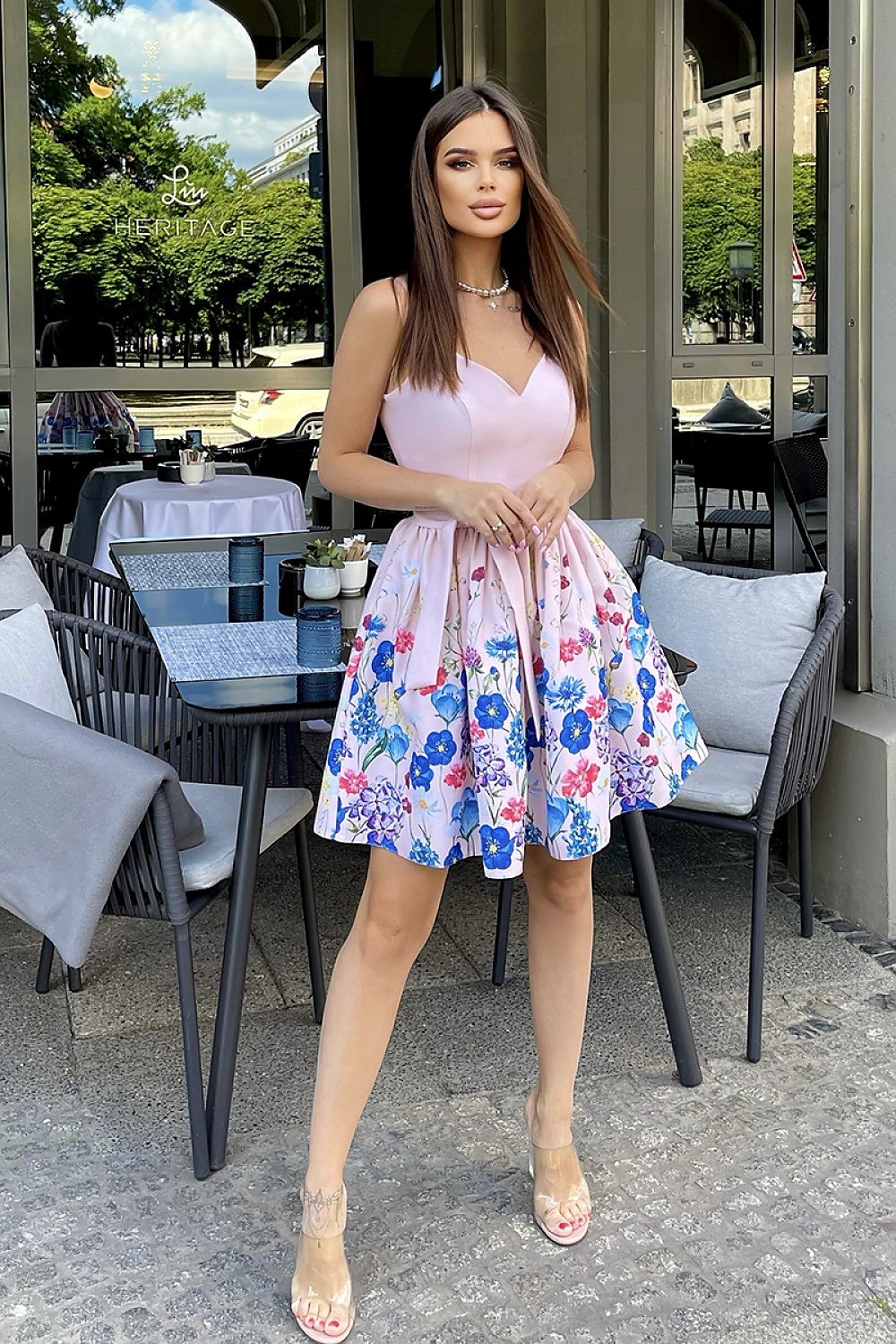 Charming woman in an Elegant Bicotone Cocktail Dress With Lovely Pastel Dyed Flowers And Flared Layered Design, posed confidently while surrounded by a luxurious outdoor environment.