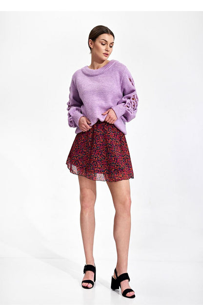 Chic model displaying the Flared Mini Skirt by Figl, featuring a flared design in a vibrant floral pattern, styled with a relaxed lavender sweater.