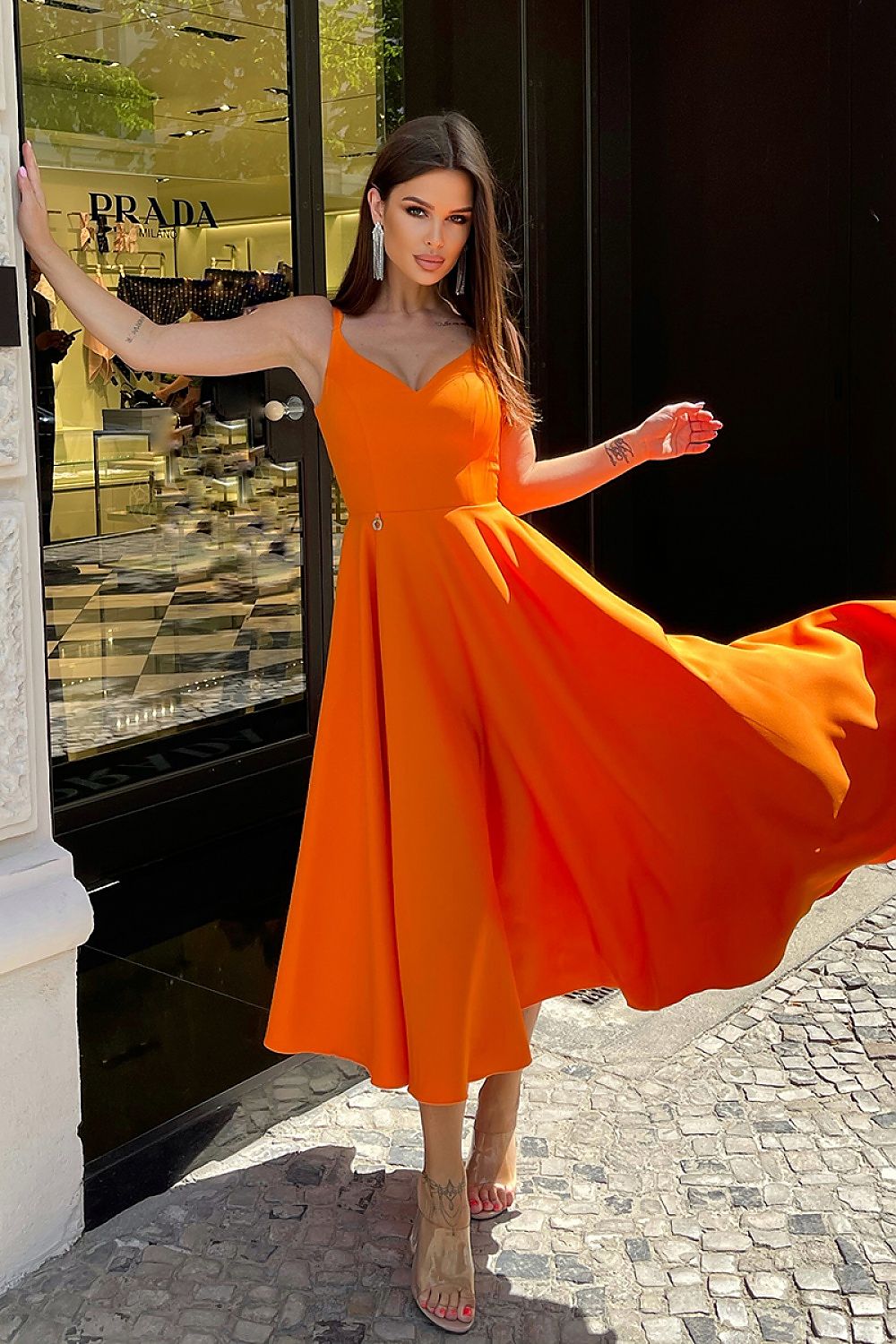 Elegant Bicotone Midi Dress with Shoulder Straps, Flared Skirt and Exposed Back - Model gracefully twirling in the stunning orange midi dress, capturing the essence of femininity and elegance against a designer storefront.
