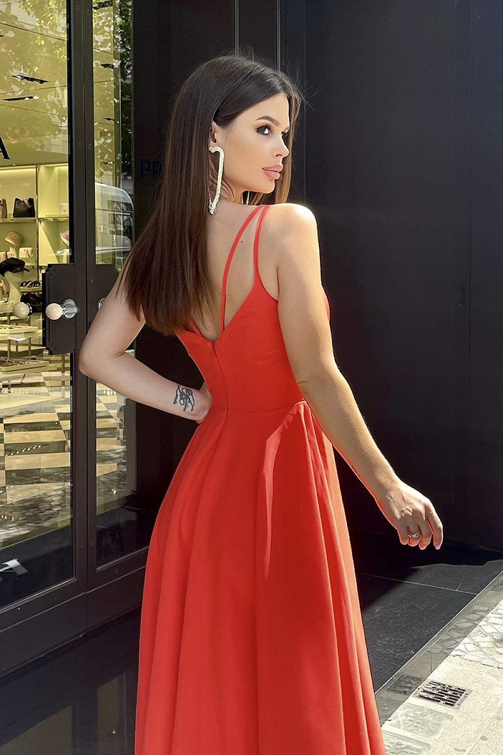 The back view of an elegant Bicotone midi dress with shoulder straps and a flared skirt, showcasing exposed back details as the model poses outside a high-end boutique.
