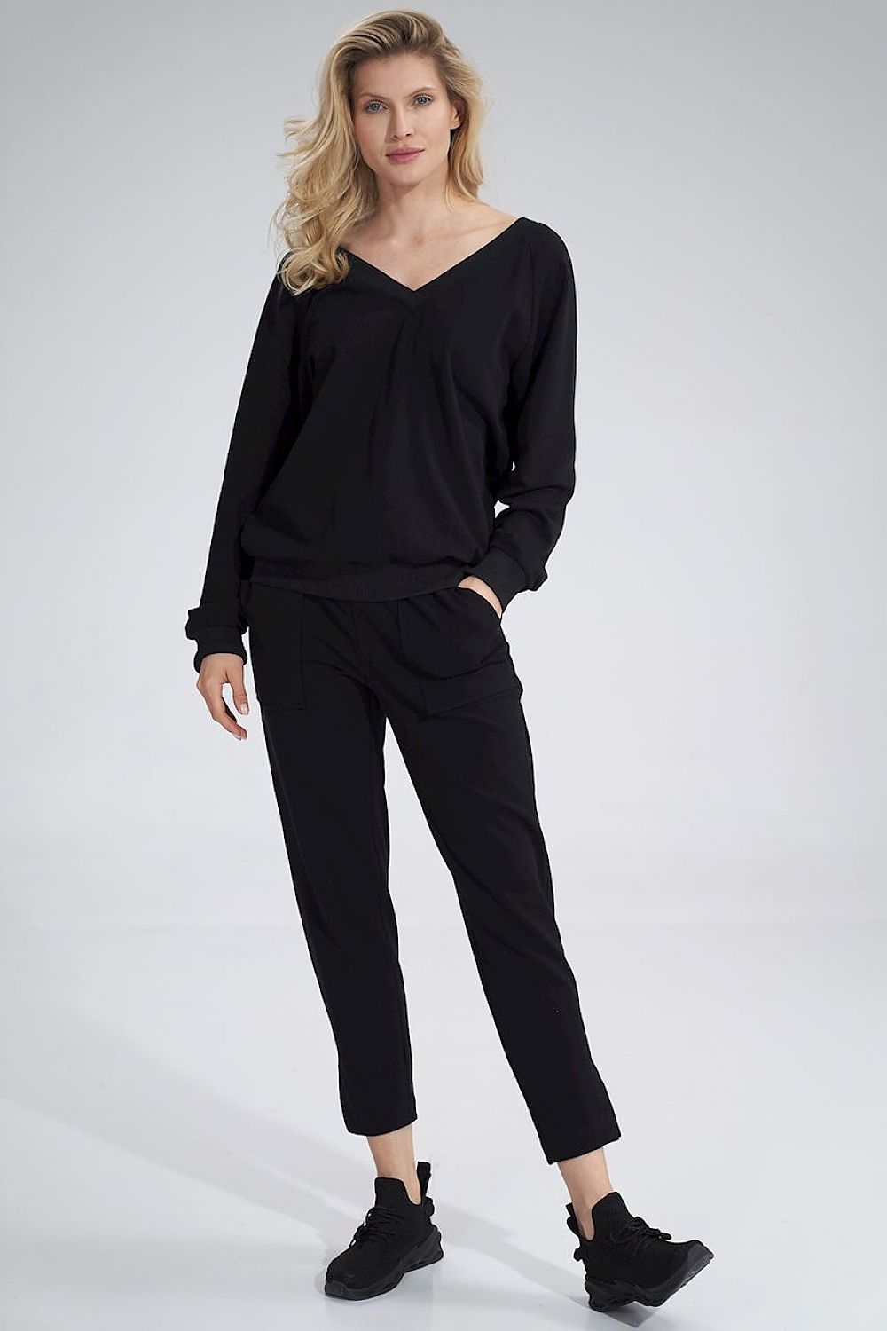 Luxury Figl V-Neck Cotton Blouse with Decorative Ribbon, showcasing a model confidently wearing black attire, including long sleeves and ribbed hem trousers.