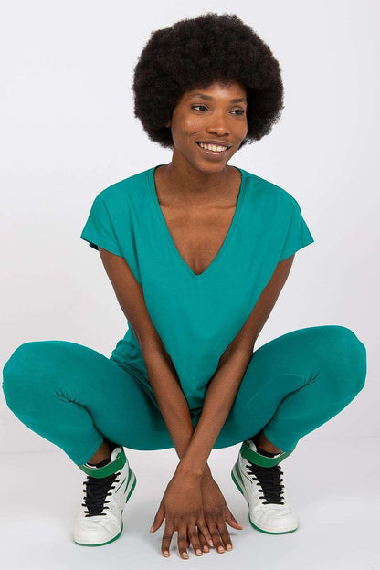 Luxury BFG Heart Neckline T-Shirt in brilliant turquoise, model squatting and radiating joy, highlighting the soft cotton blend and elegant design. Available in sizes S to XL.