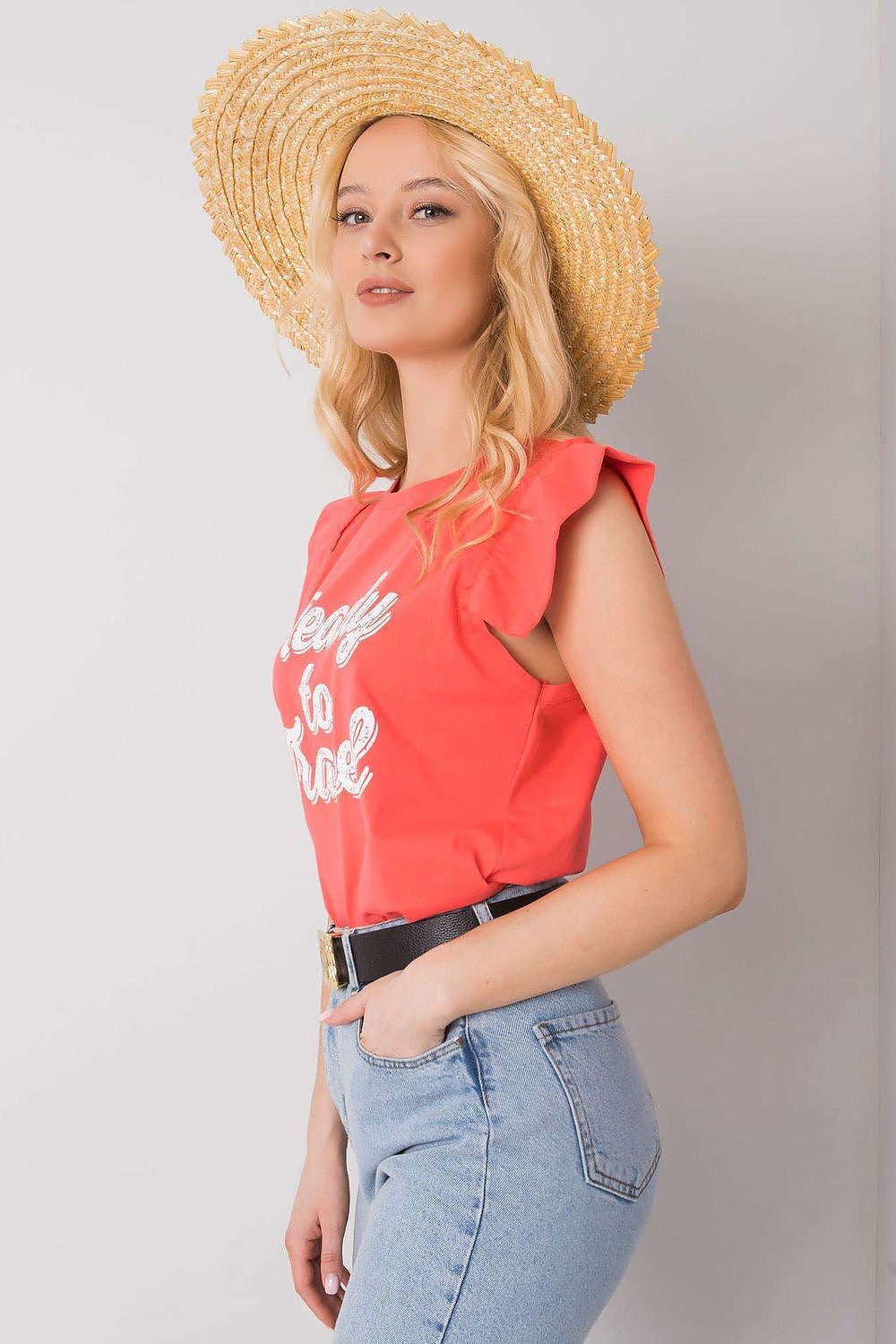 Elegant Short Sleeve Frill Blouse with Decorative Inscription - Cotton and Lycra Blend, depicting a model in a side profile, wearing a coral blouse with frills and a 'Ready to Travel' inscription, paired with casual blue jeans and a straw hat.