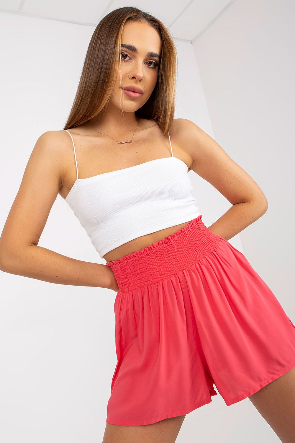 Luxurious women's high-waisted loose fit shorts in 100% viscose, showcased in a chic coral hue, paired with a stylish cropped white top for a trendy summer look.