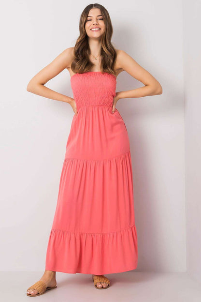 Elegant Strapless Long Summer Dress with Ruffle Hem – 100% Viscose by Fresh Made, featuring a model smiling confidently while showcasing the vibrant coral dress that has a defined elasticated top and flowing ruffle hem.