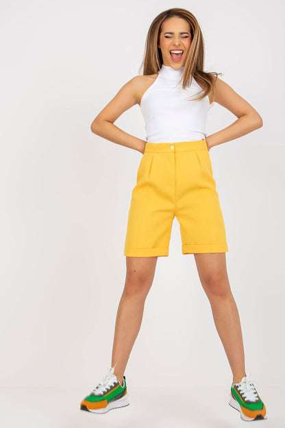 Joyful model wearing Xsapienza Higher-Waisted Shorts with Zipper Closure & Side Slip Pockets in a vibrant yellow, complemented by a white top and stylish sneakers.