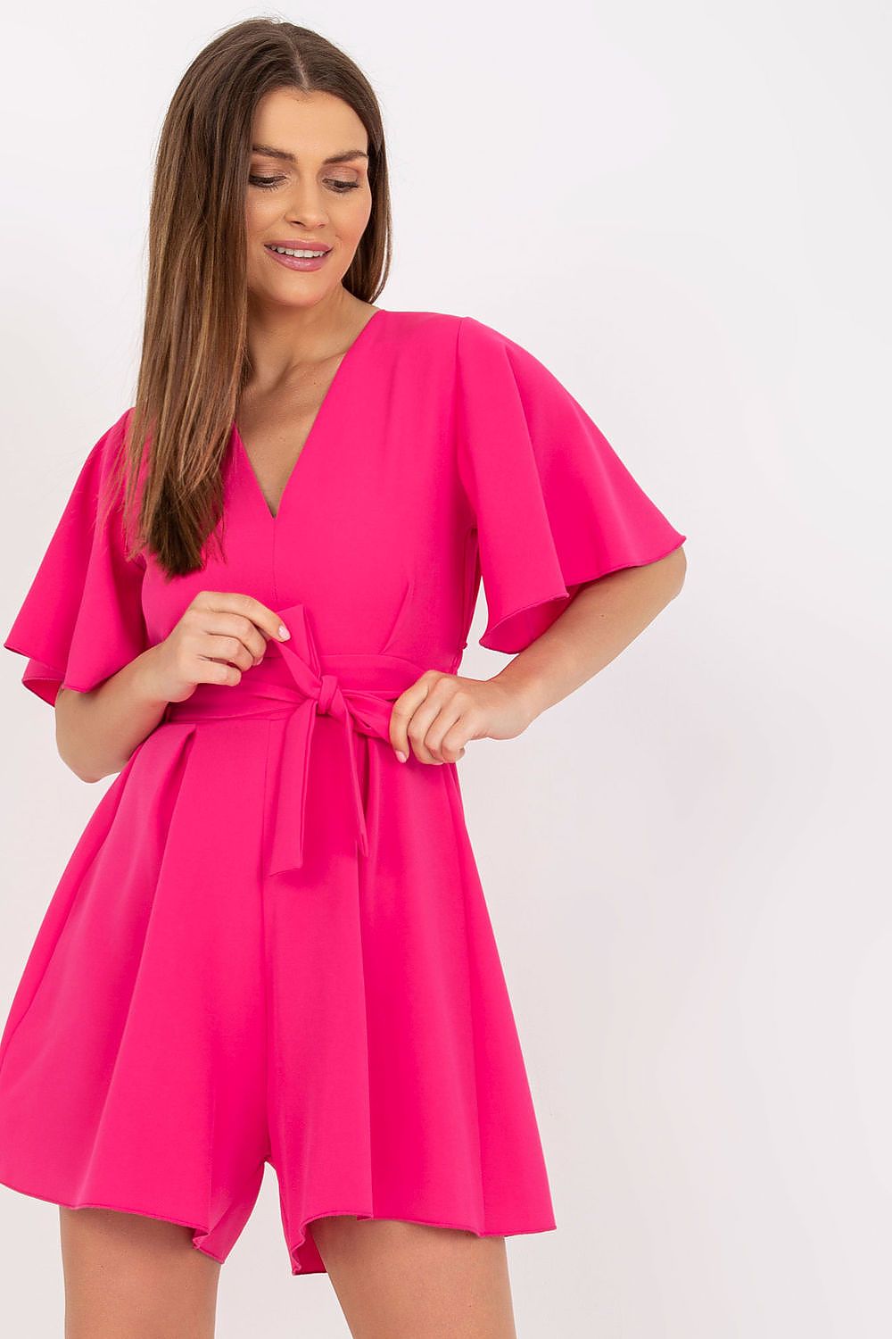 Elegant Rue Paris Jumpsuit With Cheeky Neckline And Tied Waist, showcased by a model with long hair, wearing the vibrant pink jumpsuit that features wide short sleeves, perfect for any occasion.