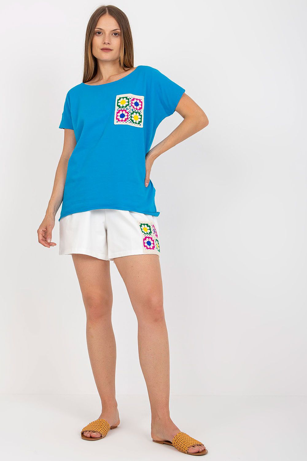 Elegant summer set featuring a vibrant blue embroidered blouse with short sleeves and an extended back, paired with stylish white wide-leg shorts adorned with floral embroidery. Perfect for a luxurious summer outfit.