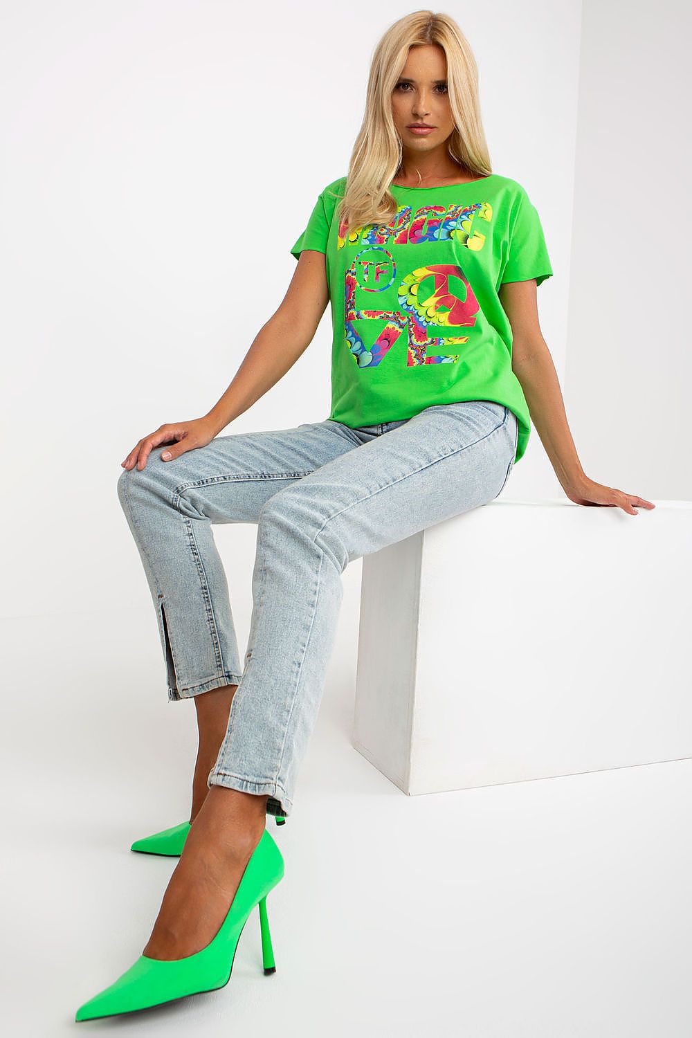 Close-up of a Model showcasing the Elegant Straight Cut Cotton Spandex Blouse with Decorative Print – Short Sleeves, EU Size 0, sitting confidently in light blue jeans and striking green stilettos, perfect for a luxurious casual look.
