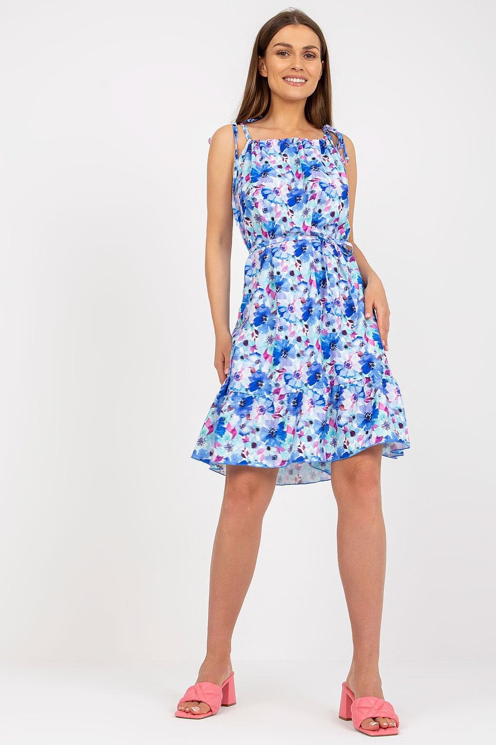 Elegant Summer Dress by Rue Paris with Colorful Pattern, Tied Straps, and Flattering Ruffles, model posing confidently in a stunning blue floral dress with a flirtatious flared hemline.