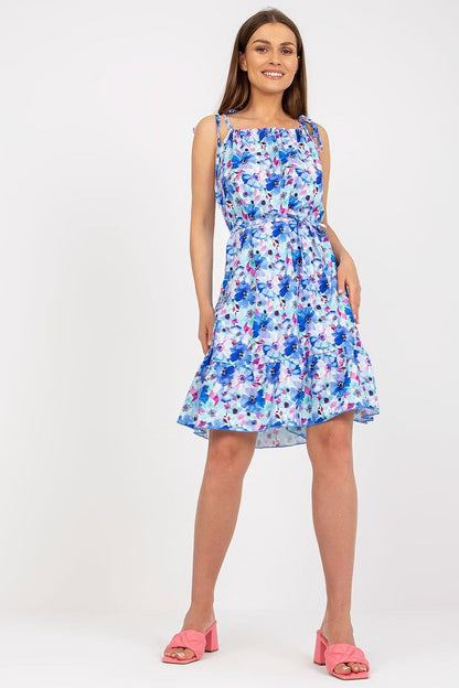 Elegant Summer Dress by Rue Paris with Colorful Pattern, Tied Straps, and Flattering Ruffles, model posing confidently in a stunning blue floral dress with a flirtatious flared hemline.