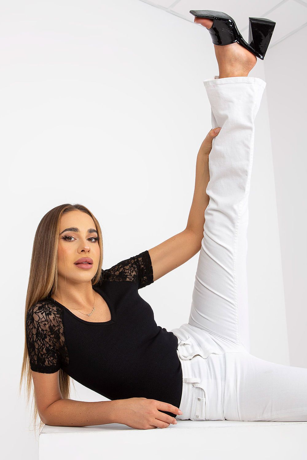 Elegant Rue Paris Blouse with Lace Short Sleeves and Heart Neckline showcased in a stylish pose, featuring a model with black lace short sleeves and white fitted trousers, radiating sophistication.