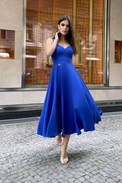 A stunning model in an elegant Bicotone midi dress with shoulder straps and a flared skirt, elegantly posed in front of a luxury boutique, radiating sophistication.