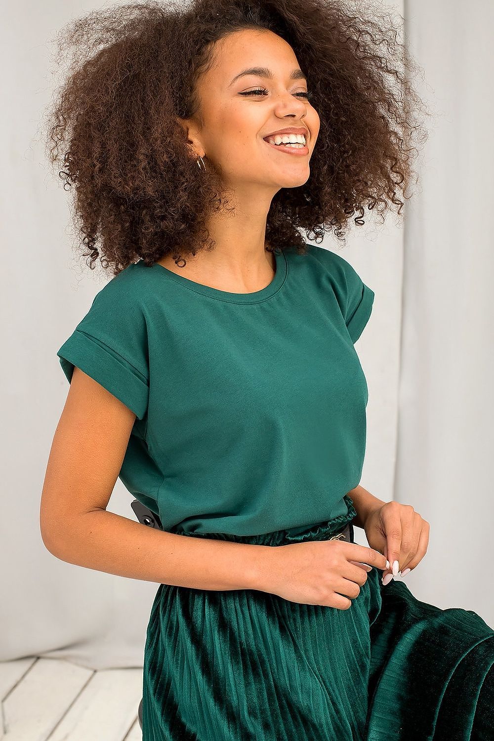 Joyful model wearing Women's Luxurious BFG Cotton Spandex T-Shirt in lush green, styled with a pleated velvet skirt, radiating elegance and sophistication.