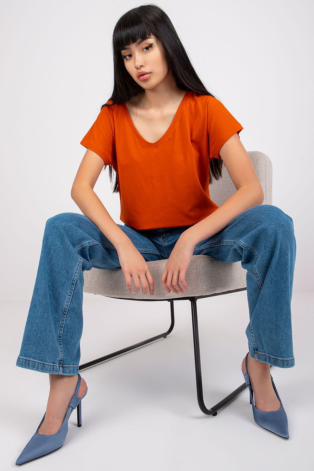 Sophisticated pose featuring the Elegant Women's Short Sleeve T-Shirt with Heart Neckline in striking orange, styled with high-waisted denim jeans.