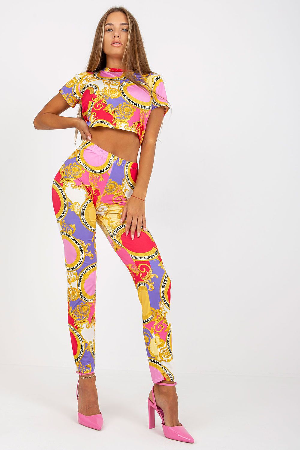Chic model wearing Italy Moda luxury high-rise trousers with an elastic waist and pockets, featuring a bold pink, purple, and gold print, highlighted with stylish pink heels.