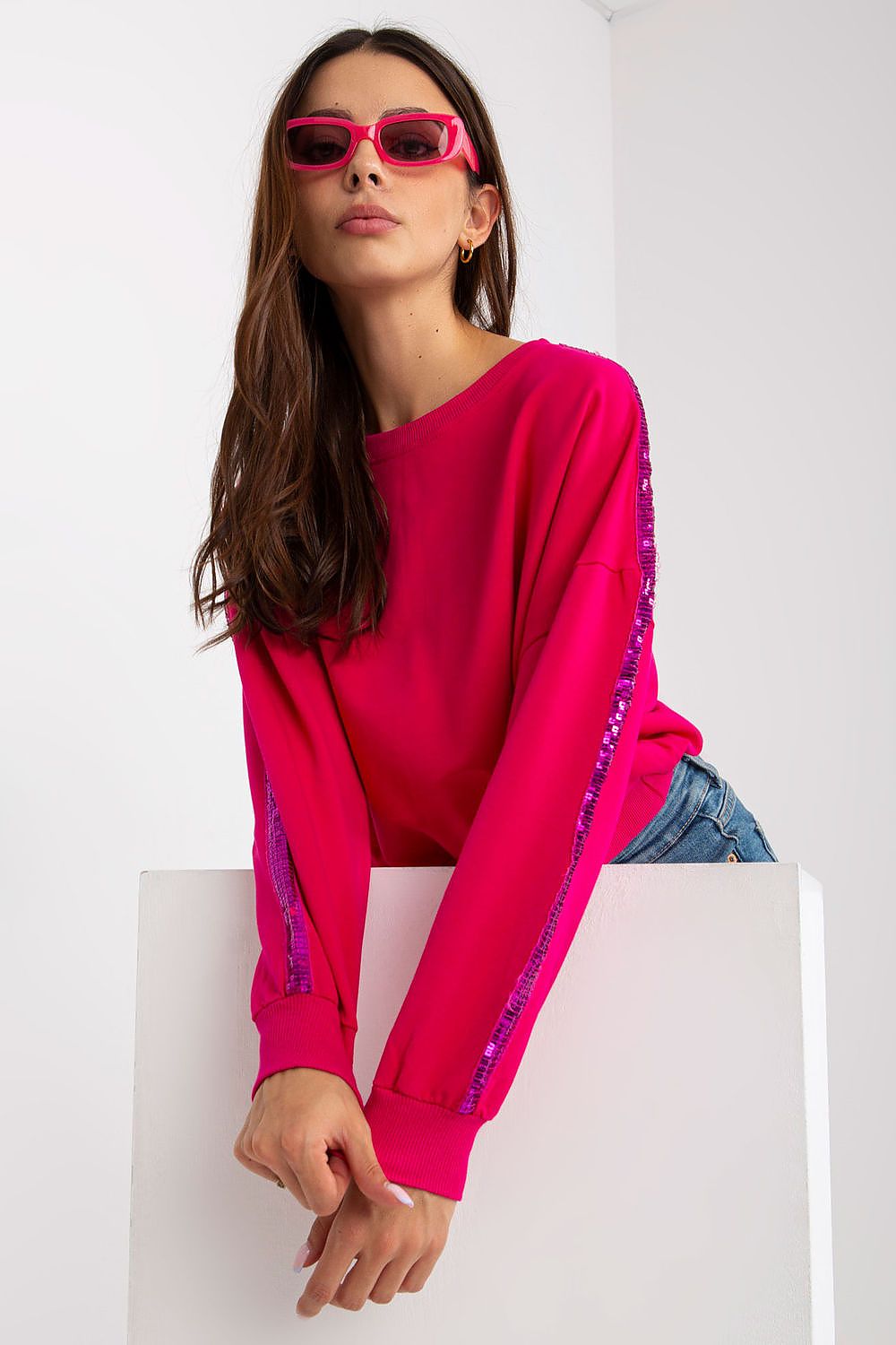Luxury Rue Paris Women's Sequined Long Sleeve Sweatshirt with Round Neckline - Elegant Comfort, showcasing a stylish pink sweatshirt on a seated model, adorned with sequins along the sleeves.