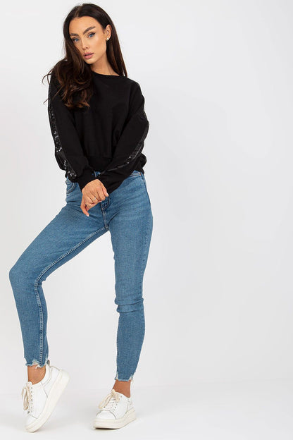 Luxury Rue Paris Women's Sequined Long Sleeve Sweatshirt with Round Neckline - Elegant Comfort, captured in a chic black version, styled elegantly on a model with blue jeans and white trainers.