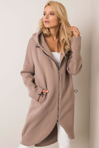 Elegant Rue Paris Zip-Up Extended Cut Sweatshirt with Hood and Side Pockets in a sophisticated taupe hue, styled effortlessly with a white top and high-fashion white trousers.