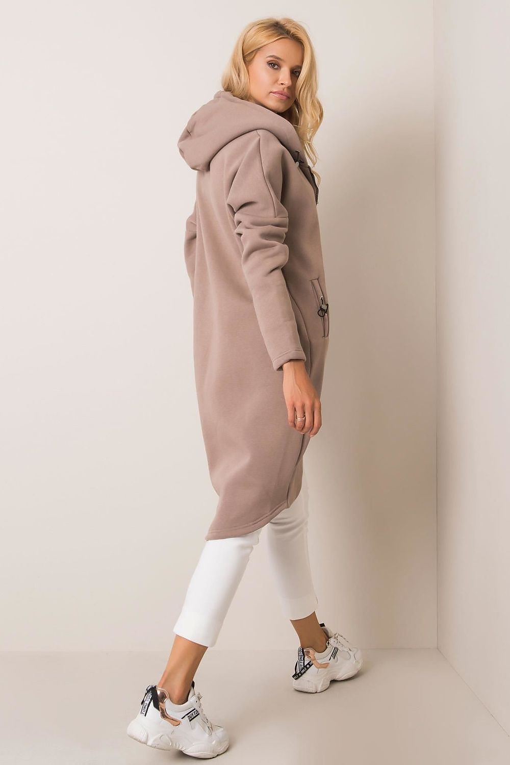 Back view of the Rue Paris Zip-Up Extended Cut Sweatshirt with Hood and Side Pockets in taupe, highlighting its luxurious fabric and chic design, paired with stylish white trousers.