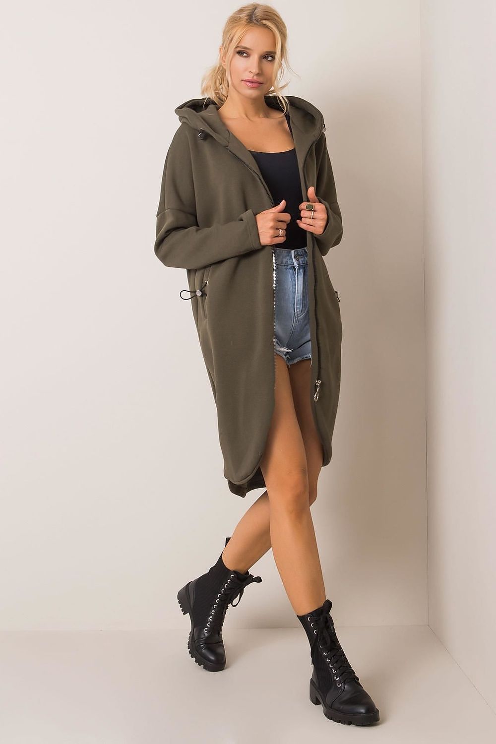 Side view of the Rue Paris Zip-Up Extended Cut Sweatshirt with Hood and Side Pockets in olive green, exuding elegance in a stylish urban setting.