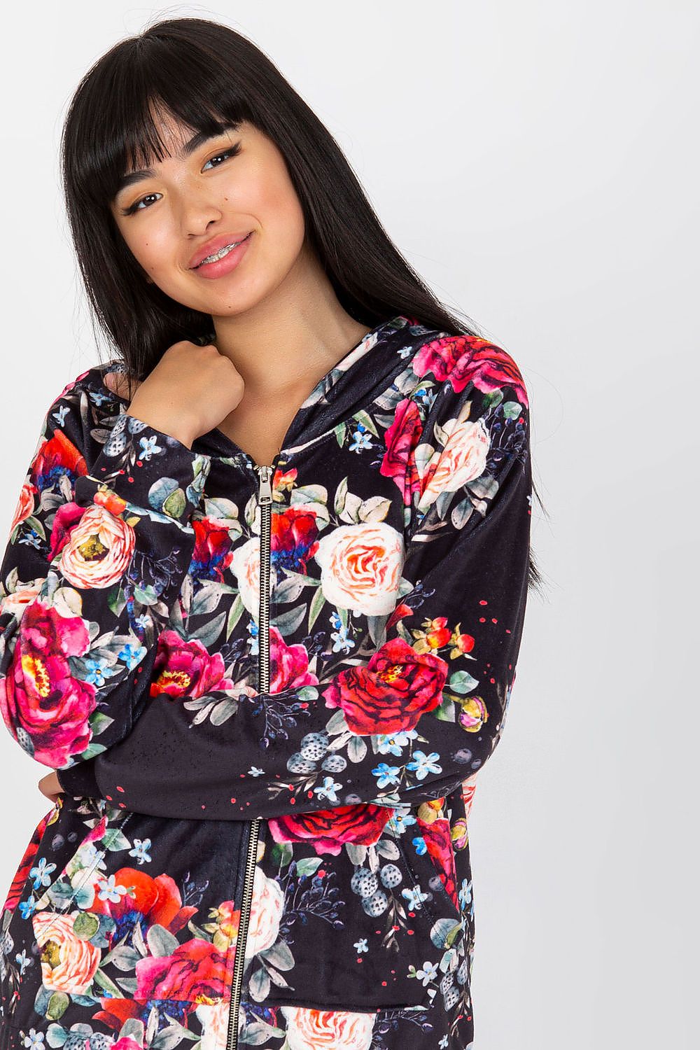 Smiling model in Luxurious Rue Paris Women's Hooded Zip Sweatshirt with Pockets, showcasing a rich floral pattern in dark hues, offering stylish comfort and available in sizes S/M & L/XL.
