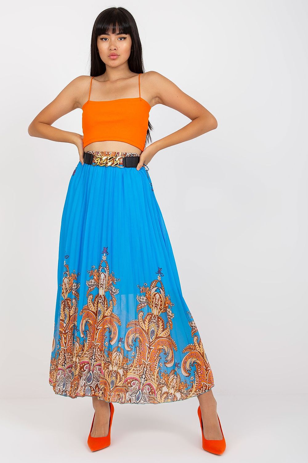 Elegant long skirt with elastic waistband and a decorative chain belt by Italy Moda, model showcasing vibrant blue skirt adorned with intricate patterns, paired with a stylish orange crop top and high heels.