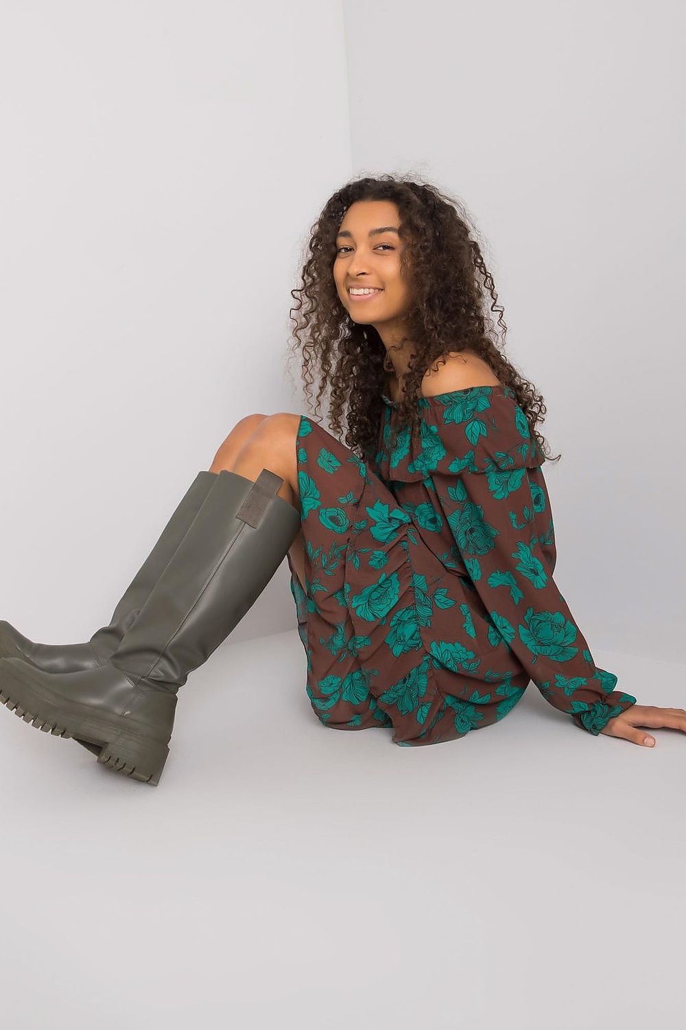 Elegant Long Sleeve Dress with Frill Hem and Spanish Neckline by Italy Moda, illustrated by a seated model in a brown dress with striking teal floral designs, exuding relaxed elegance.