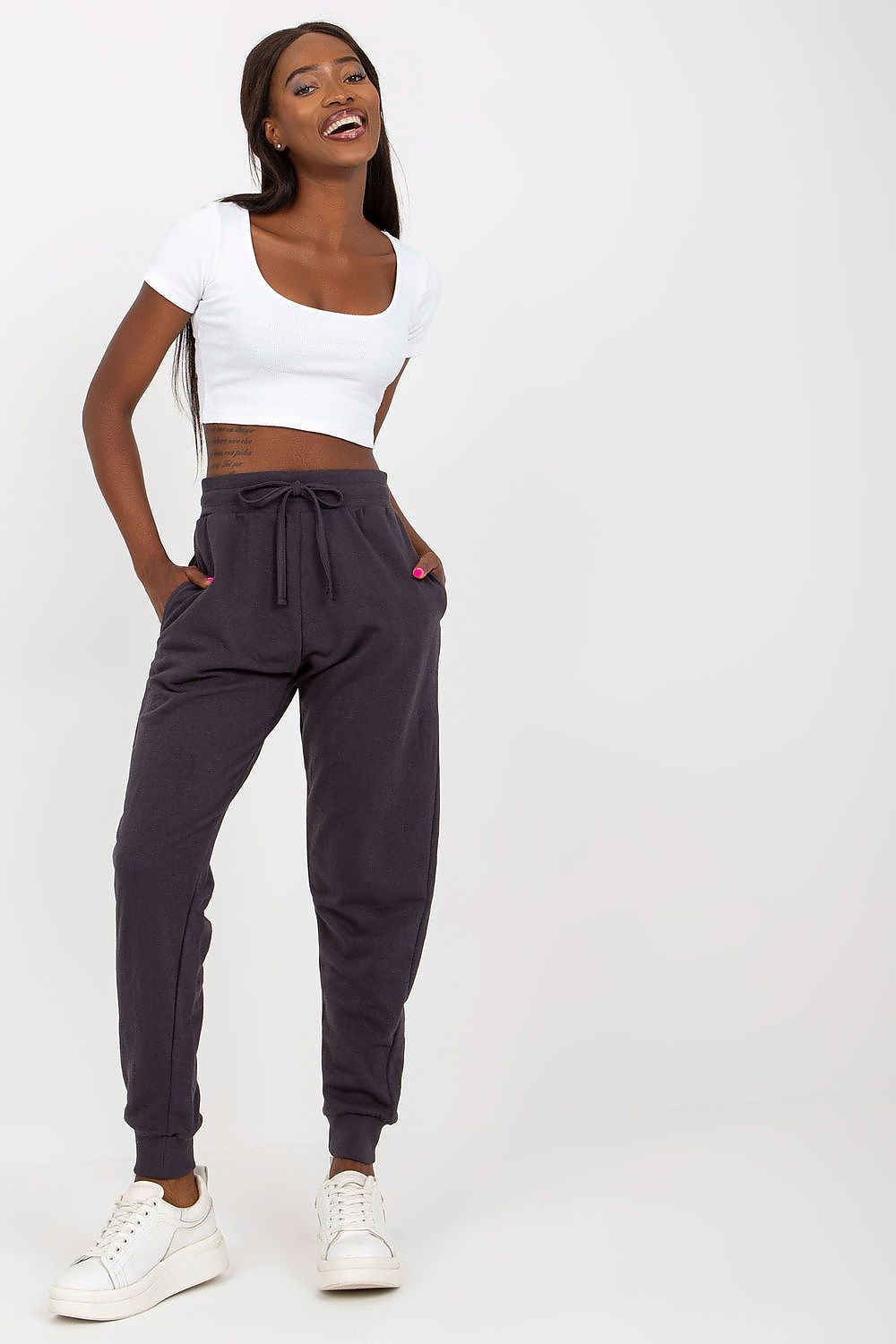 Charming model smiles while wearing BFG High-Waisted Tracksuit Trousers with Elastic Waistband and Side Slip Pockets in luxurious dark grey, paired with a stylish white crop top for a chic ensemble.