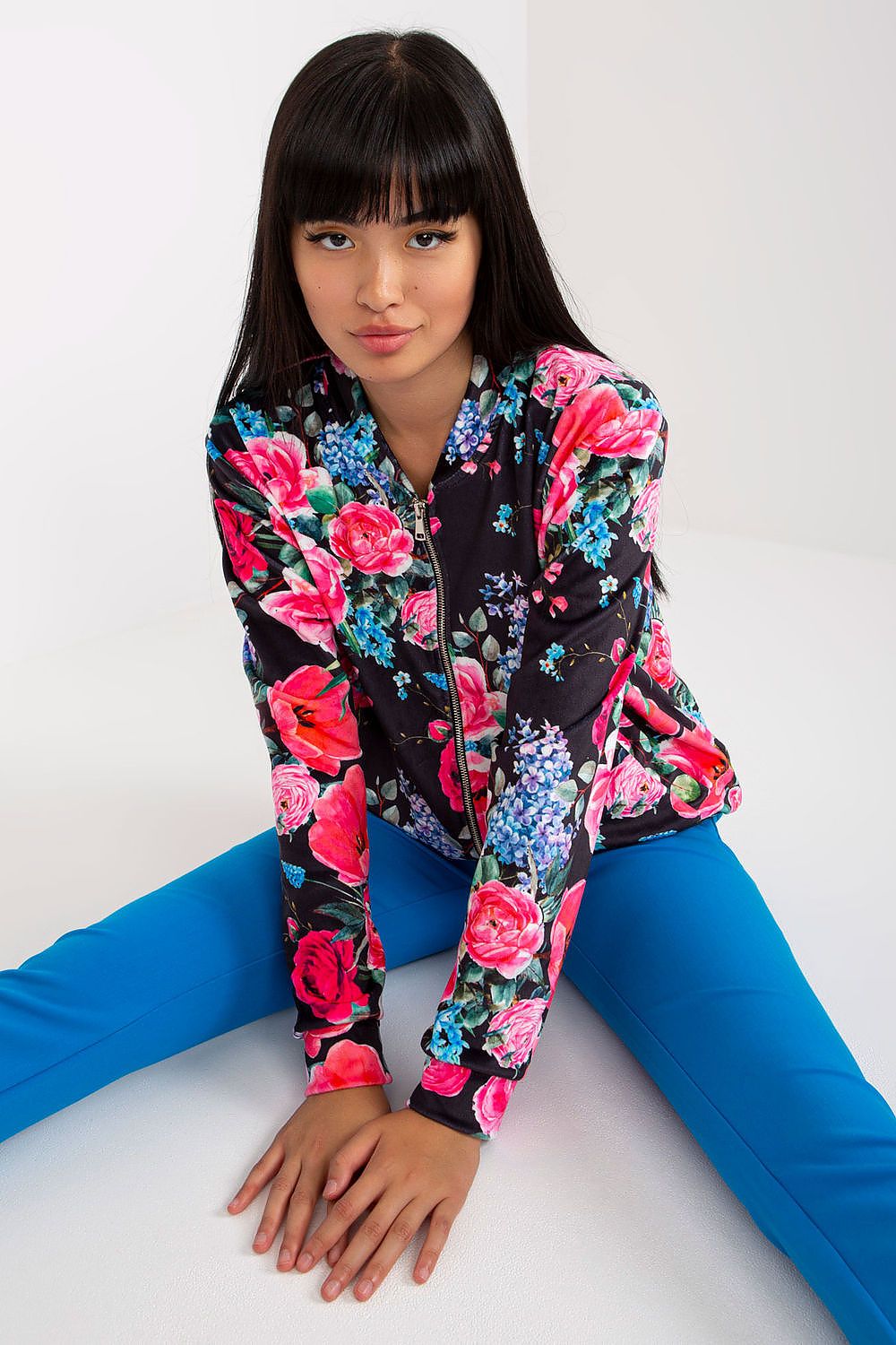 Fashionable model seated in a Luxurious Women's Zip-Up Sweatshirt by Rue Paris with Side Pockets, displaying a classy black floral design.