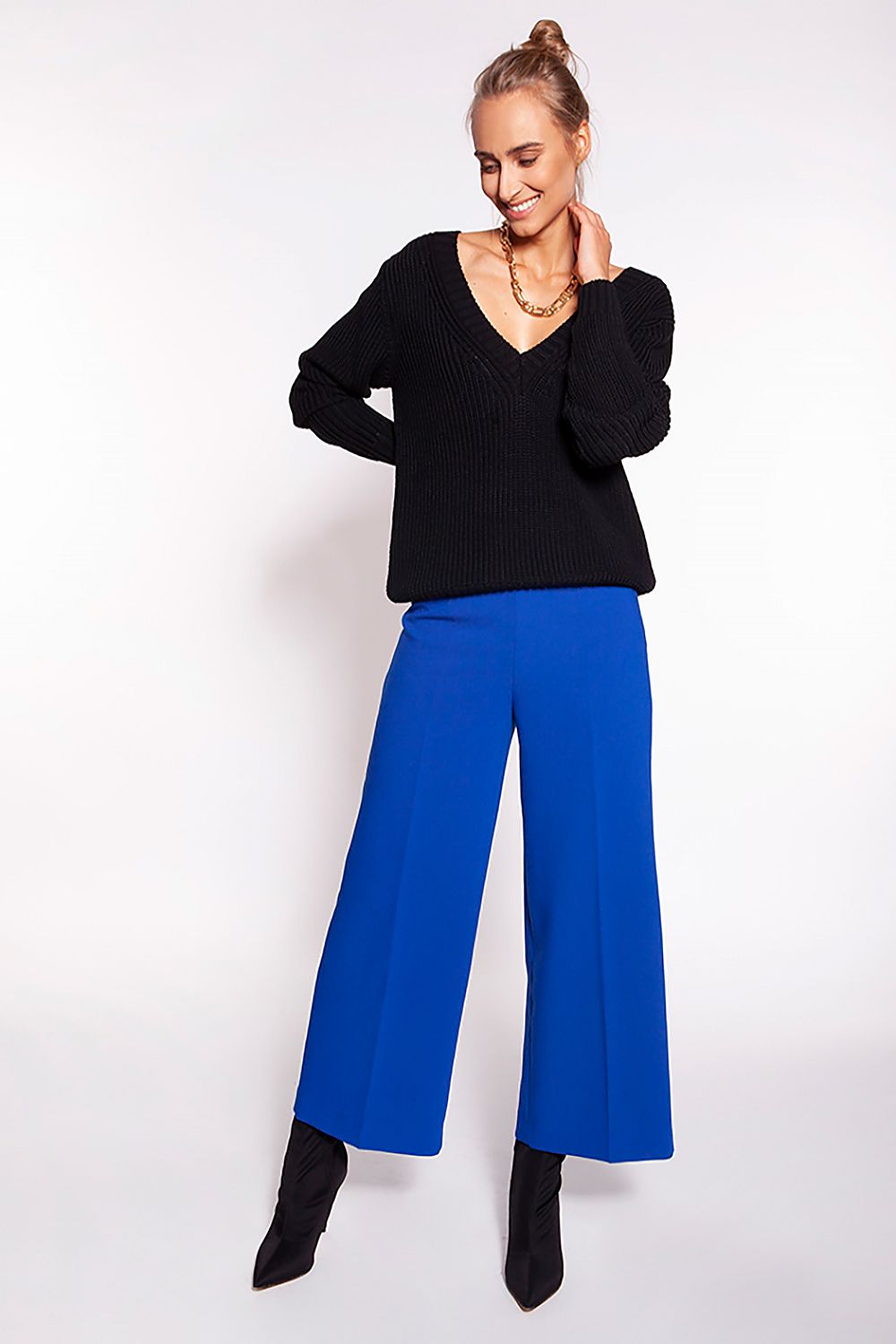 Luxurious Minimalist Ribbed Knit Jumper with Deep Heart Neckline by MKM, model wears the black version of the jumper paired with vibrant blue trousers, showcasing a chic and modern ensemble.