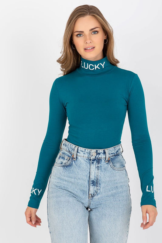 Sophisticated image of a woman showcasing the Elegant Cotton Blouse with Long Sleeves and Turtleneck by Ex Moda. The fitted style in teal features contrast lettering on the turtleneck and long sleeves, paired with high-waisted denim.