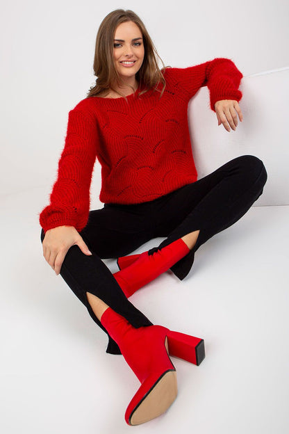 Stylish pose of a model seated in the Och Bella Openwork Sweater with Long Sleeves and Boat Neckline in bold red, complemented by chic footwear.