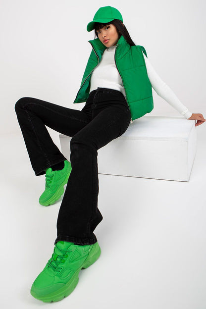 A fashionable scene featuring Och Bella Women's Insulated Quilted Vest - Short Zippered Nylon Gilet in green, complemented by stylish black jeans and matching green sneakers, epitomizing modern elegance.